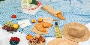 Straw Hats and Flowers Beside Fruits and Bread on Picnic Blanket
