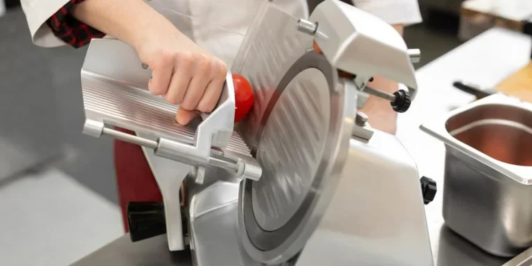 The chef in the restaurant kitchen prepares tomato slices with a slicer