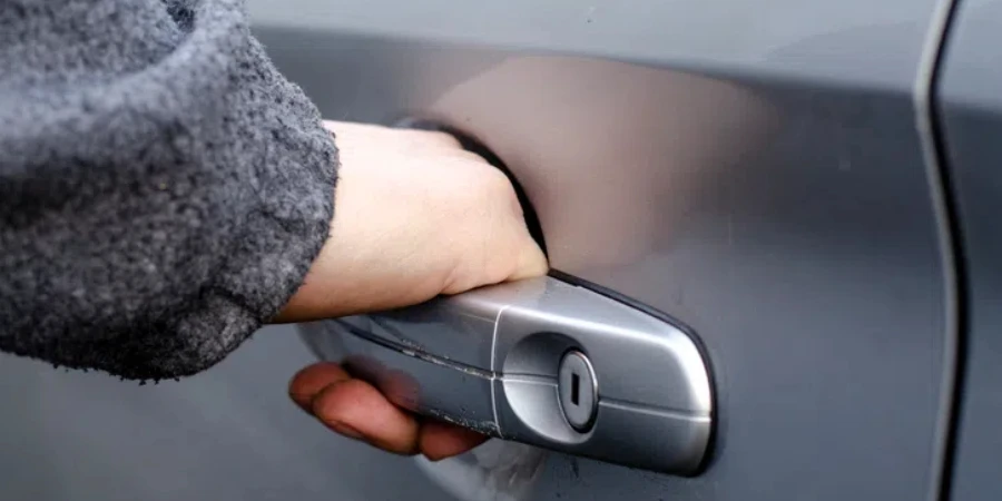 The man's hand opens the door of the silver-colored car