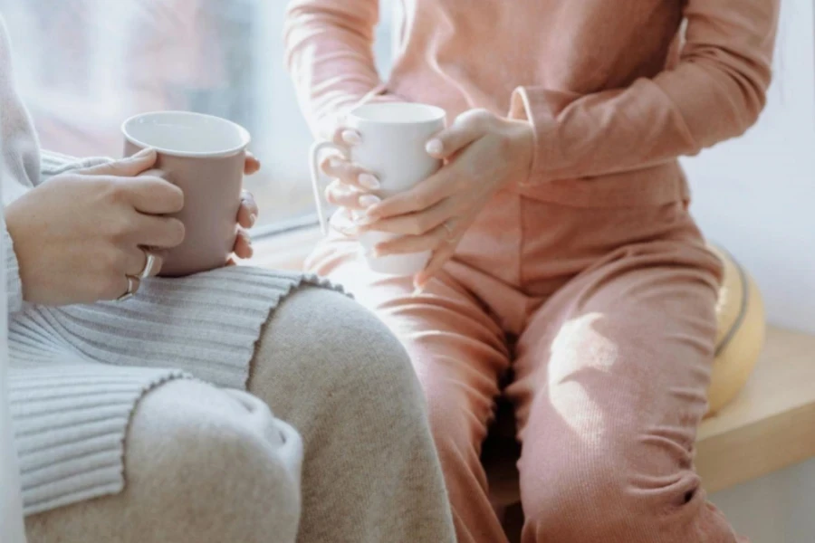 Two Persons Holding a Cup of Coffee while Sitting by the Window