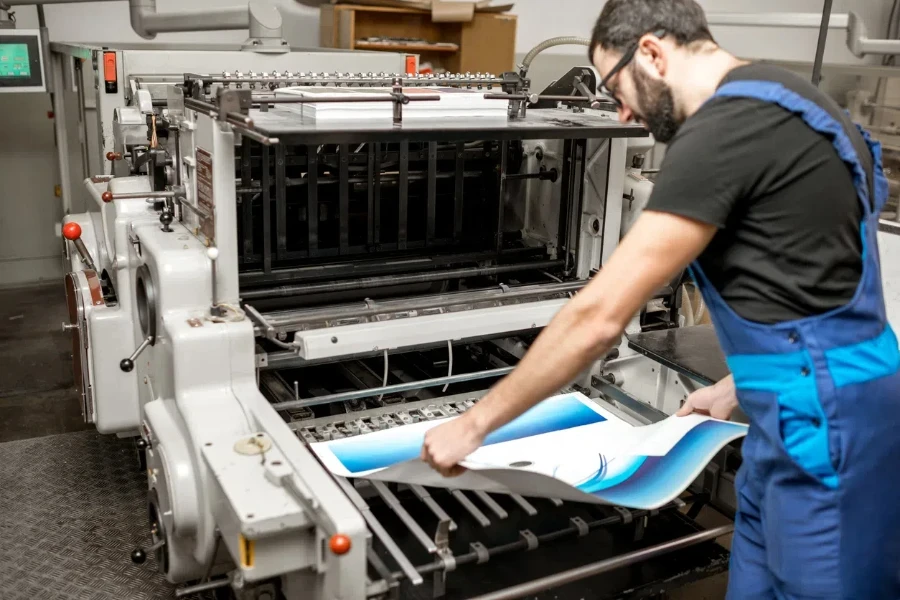 Tipografo che controlla la qualità di stampa in piedi vicino alla vecchia macchina da stampa presso la tipografia