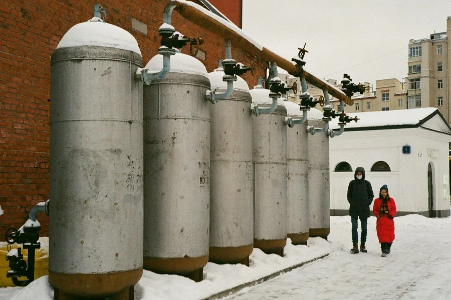 Unrecognizable couple in warm clothes walking near big industrial tanks on roof of factory on winter day