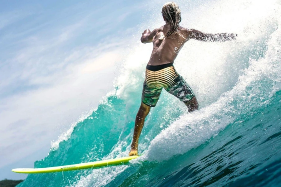 Unrecognizable shirtless sporty guy riding wave on surfboard in sunlight