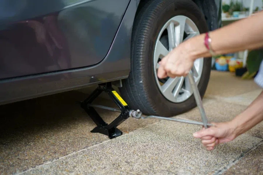 Unrecognizable woman using a car jack lifting up a car at rear wheel to change a broken or flat tyre