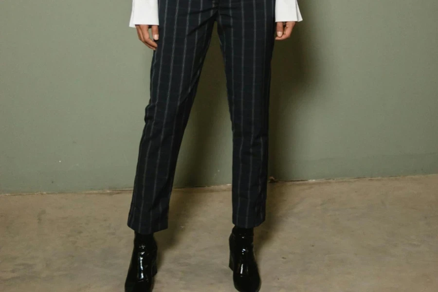 Woman Posing in White Dress Shirt and Black Pants Standing Against Gray Wall