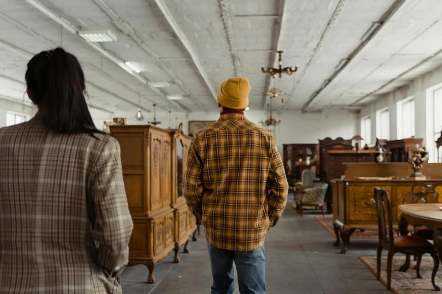 Woman in Plaid Jacket Walking Behind Man in Plaid Shirt in Vintage Store