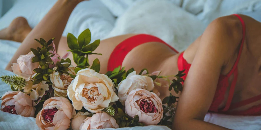 Woman in Red Two-piece Bikini Lying on Bed Beside of White and Pink Roses