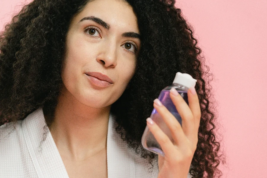 Young Woman Holding a Bottle of Makeup Remover and Smiling