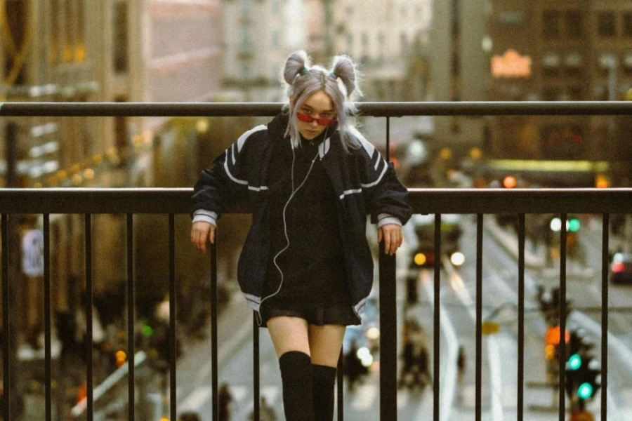 Young Woman in a Mini and Oversized Jacket with Gray Hair Tied in Ponytails Leaning on the Overpass Railing