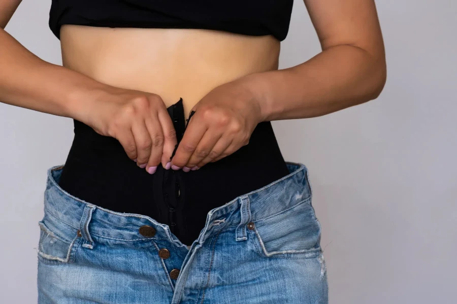 A close up of a woman wearing a waist trainer with pants