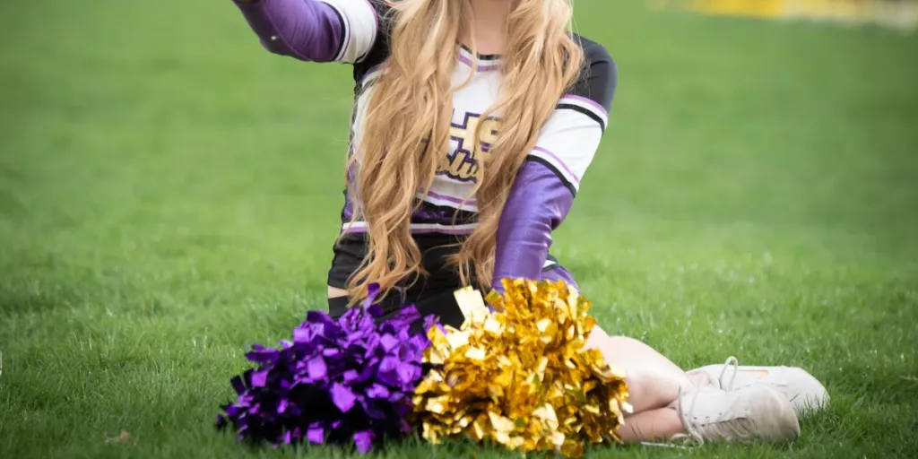 Cheerleader sitting on grass with gold and purple pom-poms