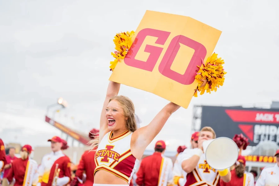 Girl in cheerleading outfit holding sign and pom poms