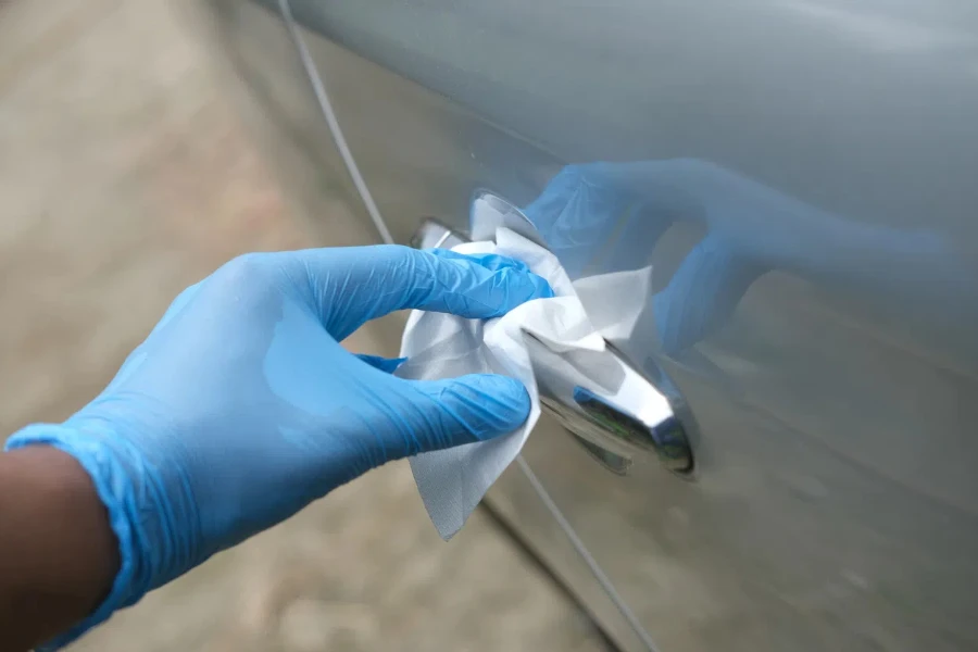 hand in gloves holding spray bottle cleaning car door