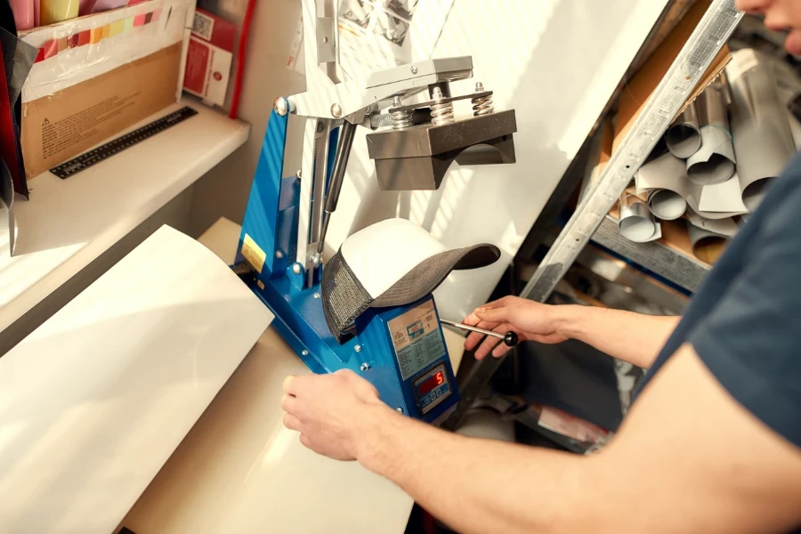 man using machine for printing on baseball cap