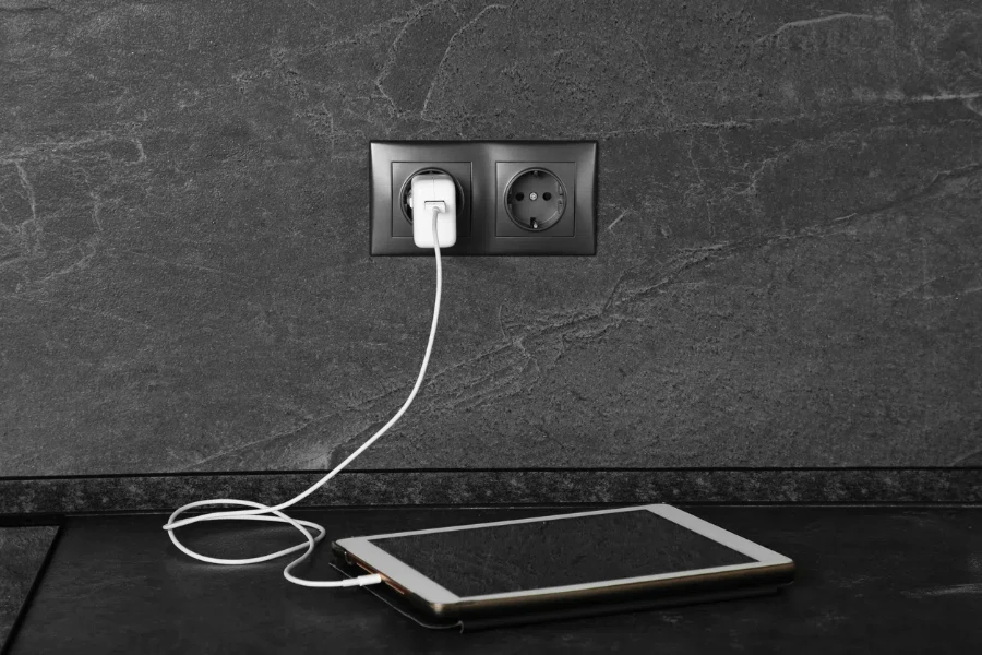 tablet charging from electric socket on dark grey table indoors