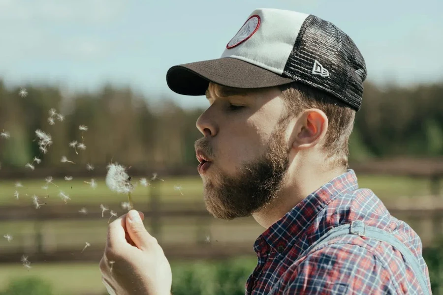 Man blowing a flower while wearing a trucker hat