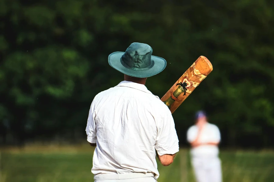 Man holding cricket bat wearing green sun hat