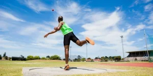 Man launching shot put ball through the air in field