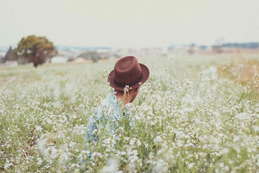 man wearing a fedora hat in a field of flowers