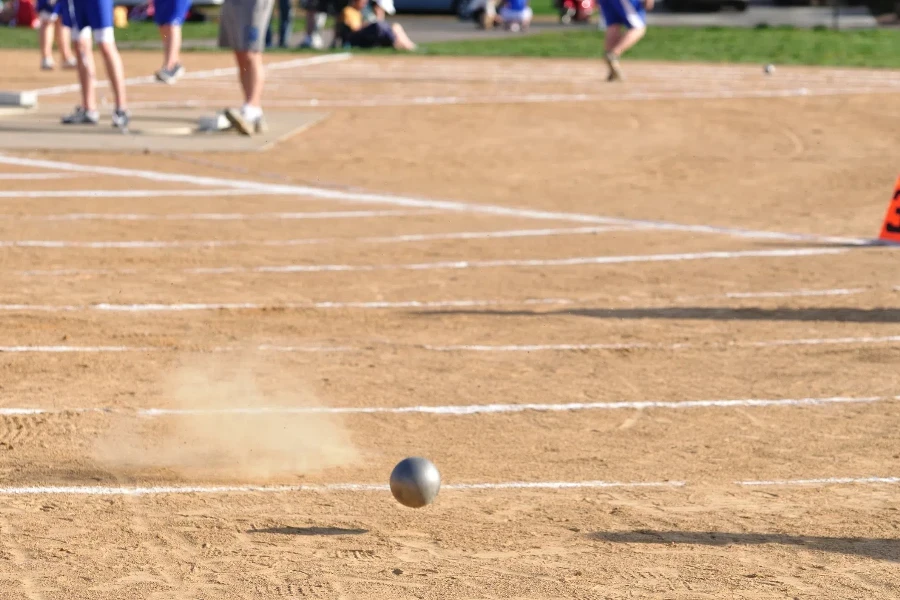 Metal shot put thrown on dirt with white markings