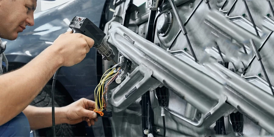 side view of car repairman holding and using the soldering iron to blend the wires