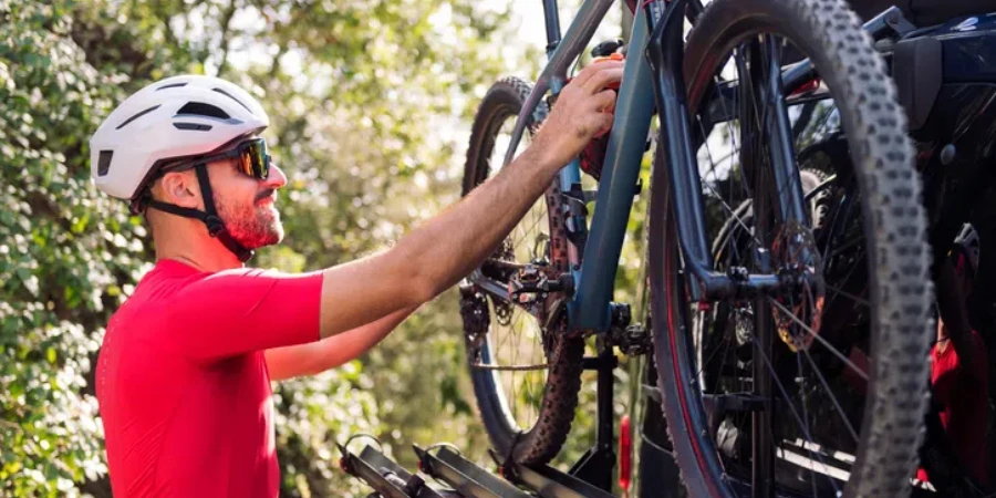 smiling young man in helmet and cycling clothes taking his mountain bike off the bike rack of his van to go for a training ride