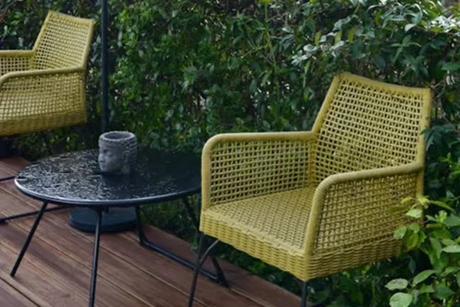 Two green rattan chairs on a deck with a table
