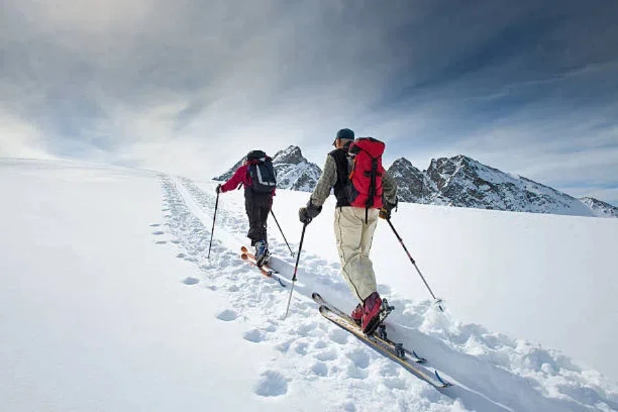 Two people going uphill on snowy slope on skis