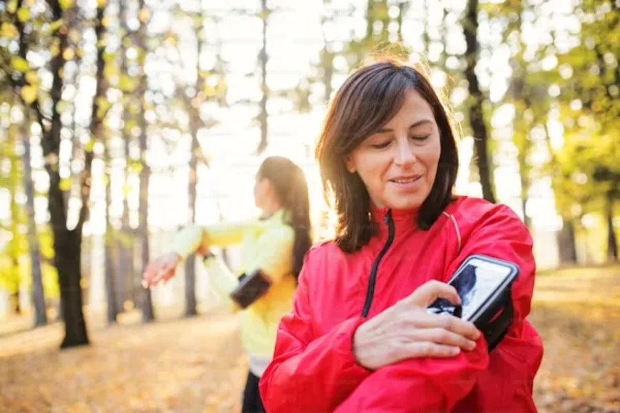 Woman connecting phone to clip-on ankle pedometer in forest