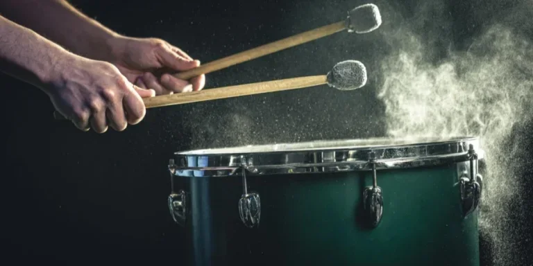 A man plays a musical percussion instrument with sticks on a dark background