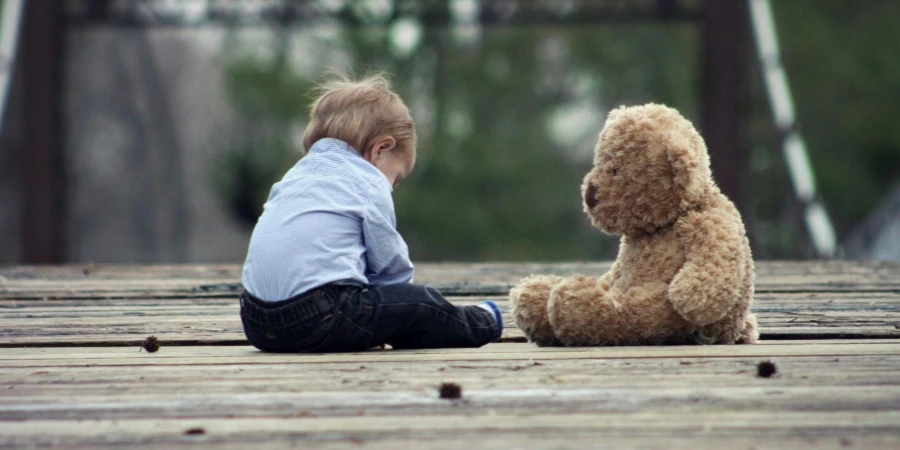 Boy Sitting With Brown Bear Plush Toy on Selective Focus Photo