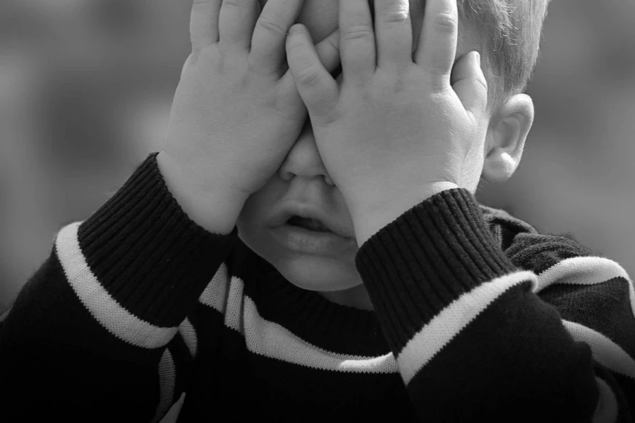 Boy in Black and White Sweater Covering His Face With His Tow Hand