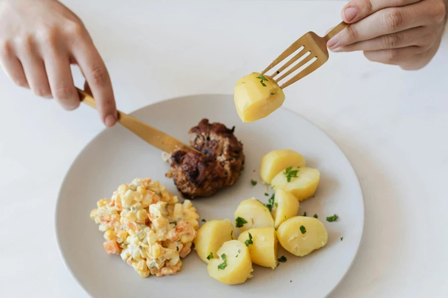 Crop person eating cutlet and potatoes with Russian salad