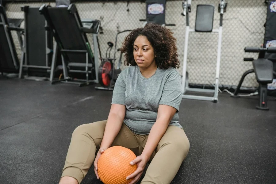 Exhausted overweight black woman resting on floor after training in gym