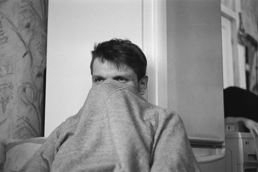 Grayscale Photo of Man Leaning on Refrigerator