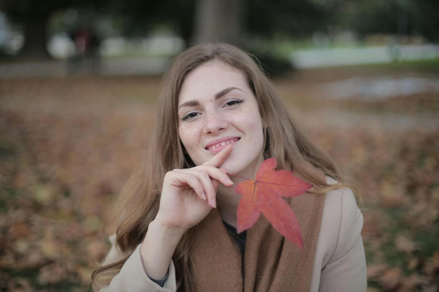 Happy Adult Woman with Red Leaf in City Park in Autumn