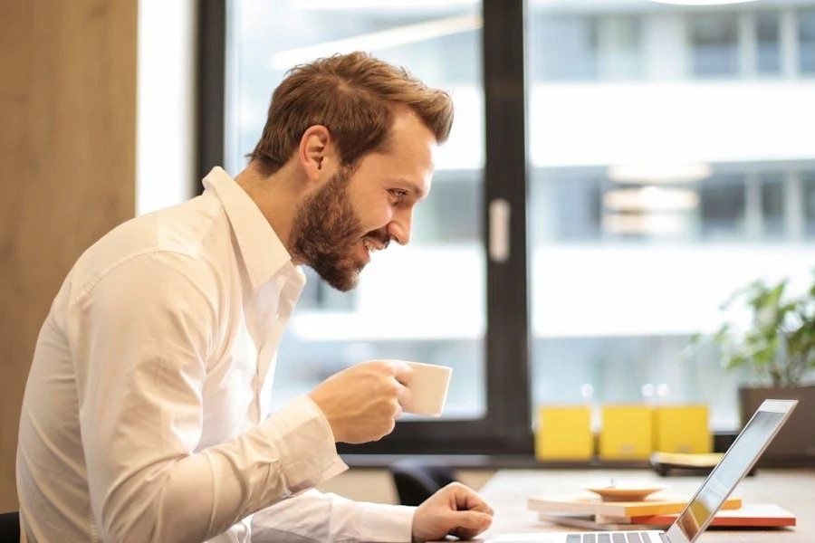 Man holding a teacup in front of a laptop