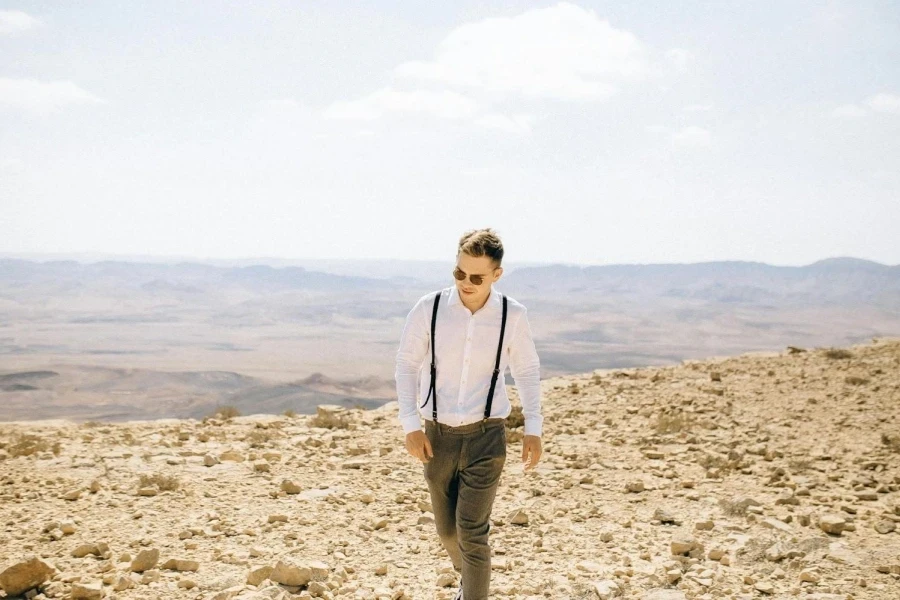 Man in White Long Sleeve Polo and Pants Standing on Rocky Sand