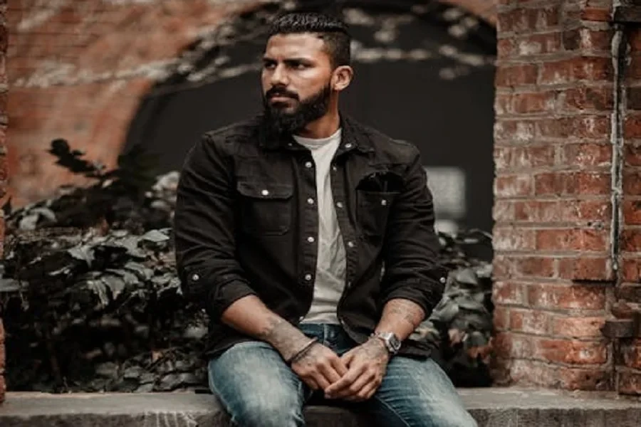 Man in black denim jacket sitting on a brick wall