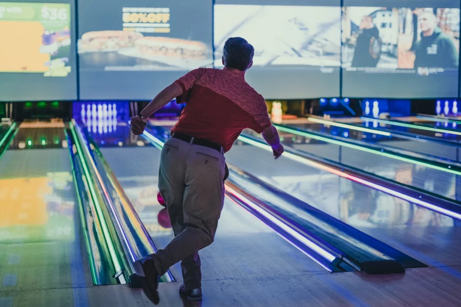 Man throwing bowling ball down alley that’s lit up