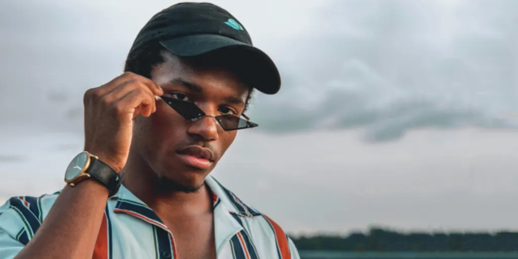 Man wearing a striped short sleeve shirt, cap, and sunglasses