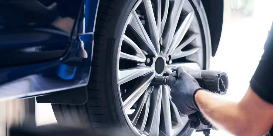 Mechanic changing car wheel in auto service using pneumatic wrench