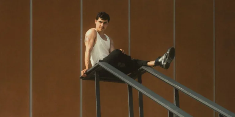 Muscular Man Wearing Tank Top Sitting on Staircase Railing Outdoors