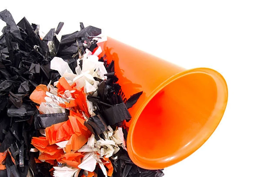 Orange plastic cheerleader megaphone next to pom poms