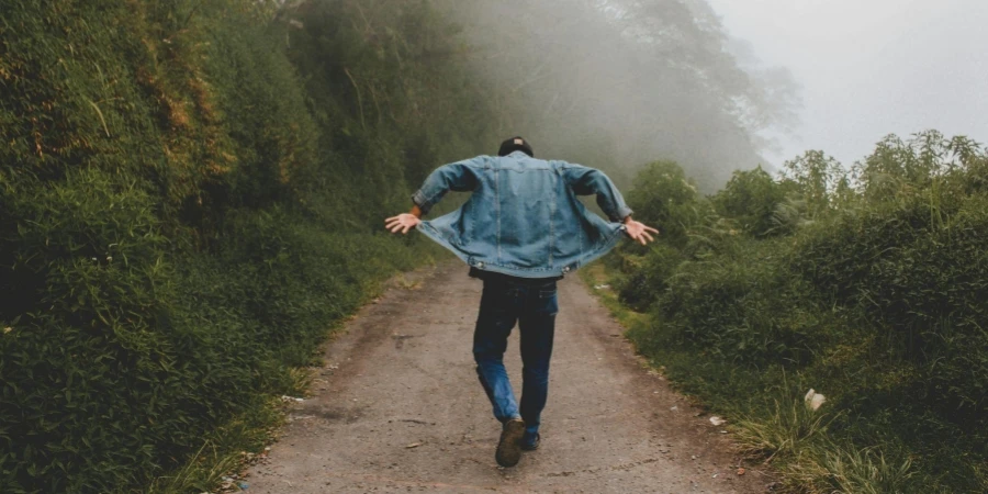 Person Wearing Blue Denim Jacket While Walking on Foggy Road