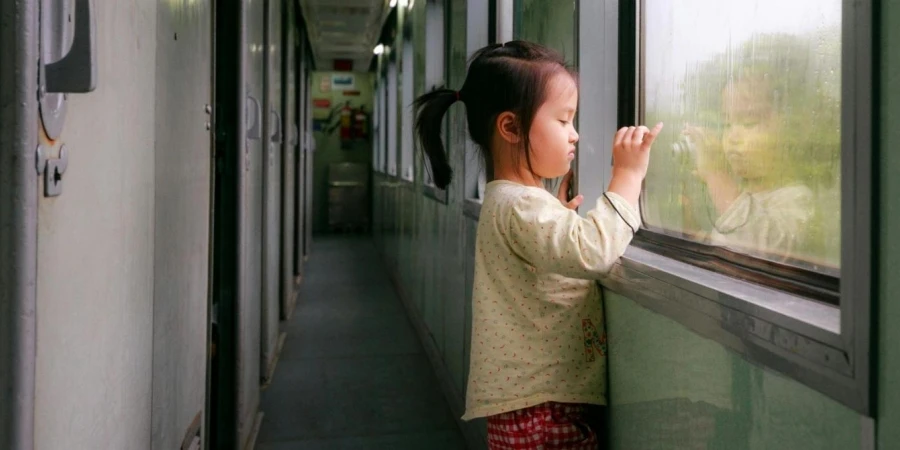 Photo of Girl Standing by Window in Train Hallway Looking Outside