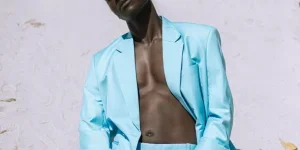 Shirtless Man in Blue Blazer and Pants Kneeling on Sand