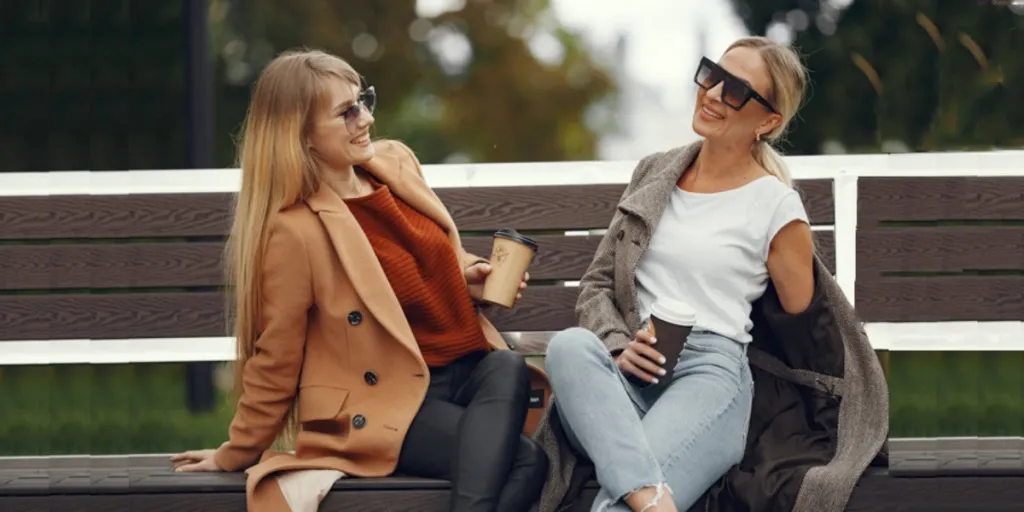 Two women on bench wearing long jackets, leggings, and jeans