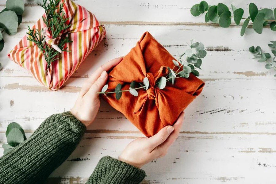 Woman holding gift wrapped in orange fabric.