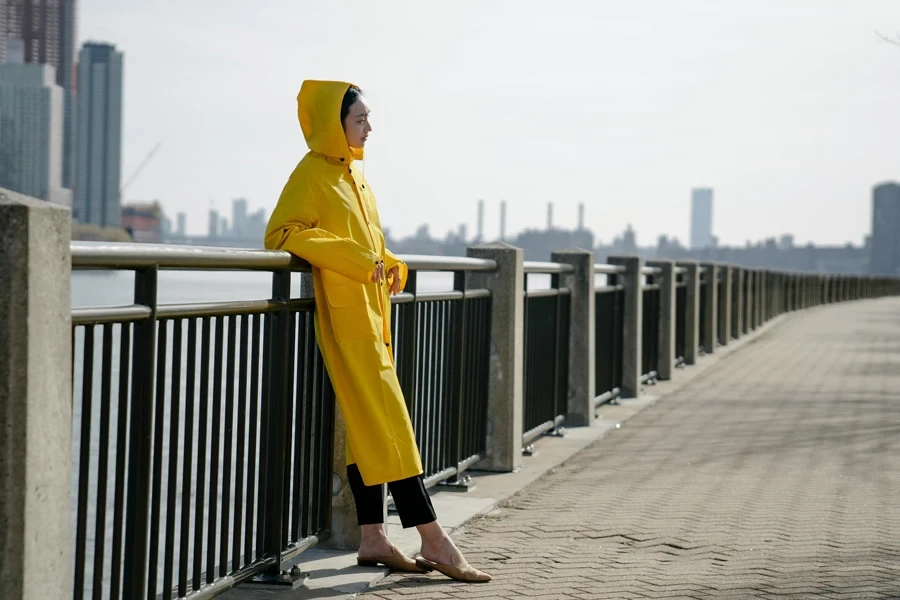 Woman in a Yellow Raincoat Standing on a Pier in City